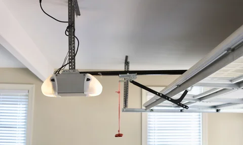 Certified garage door technician calibrating a belt-drive opener motor with ladder, safety sensors, and precision tools inside a Louisville residential garage